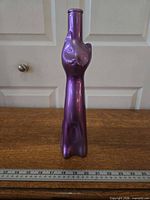 Front view of purple cat-shaped Moselland wine bottle standing upright beside ruler for scale