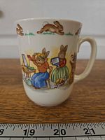 Full view of Bunnykins mug showing main illustration and ruler for scale