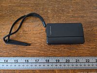 Camera with wrist strap next to ruler closed front view