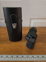 monocular standing beside closed leatherette case on ruler for scale