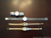 Four quartz wristwatches laid out horizontally showing different band styles and dial colors.