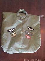 Green Krauter helmet bag with six assorted paratrooper wing badges arranged on the front