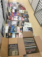 Two open cardboard boxes of vinyl LP records arranged in rows on a storage facility floor