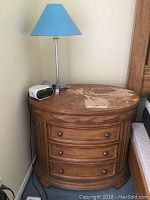 Photo of one of the oval end tables showing three drawers, surface wear and a blue lamp and alarm clock on top.