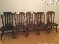 Front view of five wooden chairs lined up with one captain's chair with arms and one darker wood chair