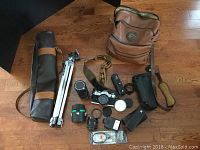 Overview of all items including Canon AE-1 camera, lenses, tripod, flash, accessories, and camera bag on wooden floor.