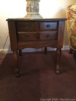 Front view of one wooden end table showing four drawers and turned legs.
