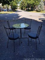 Photo showing full patio set from above with table and four chairs outside on paved driveway with trees and street in background.