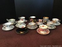 Front view of vintage tea cups and saucers arranged in two rows showing variety of patterns and colors