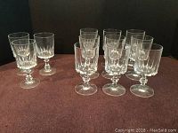 Overall lot photo showing two groups of clear crystal glasses with faceted stems and vertical cuts, one group of 9 and one group of 3 glasses.