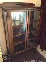 Front view of wooden curio cabinet showing glass doors and wood detail on top.