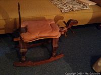 Angled front-side view of wooden camel saddle rocker showing leather seat cushion and rocker base