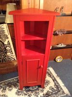 Front view of red wooden corner cabinet showing two open shelves and one door compartment.