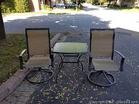 Photo showing the table with glass top and two swivel chairs from the front, outdoors in driveway with leaves scattered.