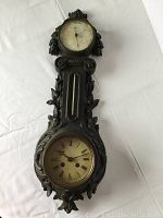 Full view of antique wall-mounted barometer, clock, and thermometer with cast metal bronze finish frame decorated with leaves and flowers.