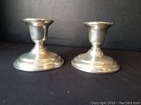 Pair of polished sterling silver candle stick holders placed side by side on black background.