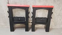Front view of two black plastic sawhorses with bright red tops against concrete wall.