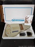 Full lot in white styrofoam packaging showing Omnichord, instruction manual, cables, and adapter
