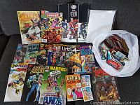 Collection of comic books and bag of sports cards displayed on a couch.
