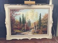 Framed oil on board forest landscape painting by E. Jalava showing birch and pine trees, pathway through autumn foliage, in ornate white frame with cracks and light fixture.