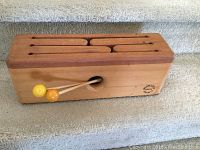 Front view of the wooden tongue drum showing the six tongues and two mallets resting on top.