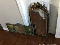 Photo showing the two vintage mirrors side by side, one ornate with gold frame and arched top, the other horizontal triptych with painted scenic panels and mirror panel.
