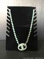 Full view of jade bead necklace displayed on black stand, showing the entire length and pendant.