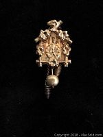 Front view of the 8K gold cuckoo clock pendant showing detailed clock face with leaves and birds motifs and hanging pinecone weights and pendulum.