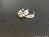 Pair of 925 sterling silver hoop earrings with three rows of cubic zirconias set along the front, shown on a black background.