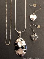 Full view of the sterling silver chain necklace with pendant and pair of heart-shaped earrings on black background.