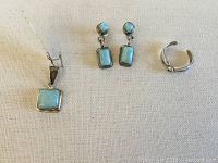 Photo showing sterling silver pendant with rectangular light blue Larimar stone, matching earrings with round and rectangular Larimar stones, and a silver open band ring.
