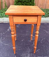 Front view of wooden side table showing top, drawer front and turned legs