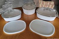 Three CorningWare casseroles with three glass lids and two plastic lids displayed on table