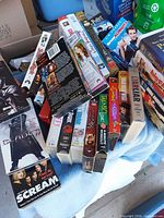Stack of assorted VHS tapes on blue blanket showing titles such as Blade, Scream and others