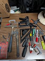 Tabletop view of entire assortment showing hammer, pipe wrench, speed square, staple gun, C-clamps, screwdrivers, pliers, bit set and accessories