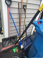 Group of snow shovels and push brooms leaning against siding