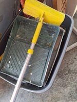 Extension pole with yellow edger head resting on green paint tray inside bin