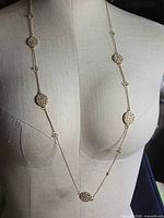 Full front view of gold-tone necklace on mannequin showing length and seven circular filigree stations
