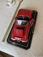 Top view of red 1:12 1958 Chevrolet Corvette model on display base with hood and driver door open, measuring tape alongside