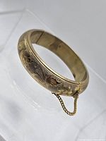 Full view of bangle showing engraved floral pattern and safety chain