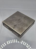 Top view of closed square compact showing engraved floral panel and textured border.