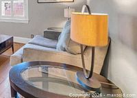Close-up of one oval end table showing glass top, dark wood frame and lamp for scale