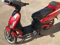 Front-left angled view of red Daymark electric scooter on center stand