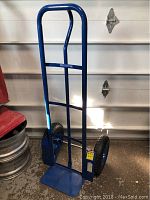 Full side view of the Westward blue steel dolly showing the frame, base platform, and tires against a garage door background.