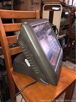 Side angle of Radiant Systems touchscreen POS computer on wooden chair showing the vented casing and device shape.