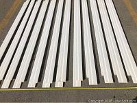 24 pieces of white primed MDF baseboard moulding laid out side by side on concrete floor, showing length and profile.