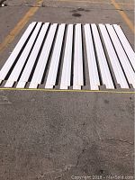 24 white primed MDF moulding strips laid side by side on asphalt surface