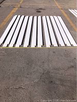 24 pieces of white primed MDF step baseboard moulding laid out on pavement, each approximately 7 feet in length.