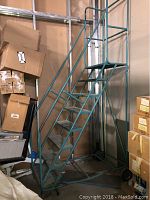 Full front view of teal rolling staircase ladder showing steps, handrails, platform and caster wheels