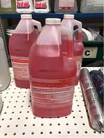 Three translucent gallon jugs labeled Retail Multi-Quat Sanitizer with a red liquid inside, placed on a shelf with other cleaning products.